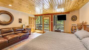 A bedroom with a large bed, a leather sofa, a television, and a fireplace.