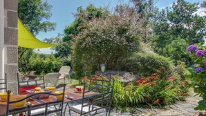 Um pátio com mobiliário de exterior, um toldo amarelo e um jardim com várias plantas e flores.