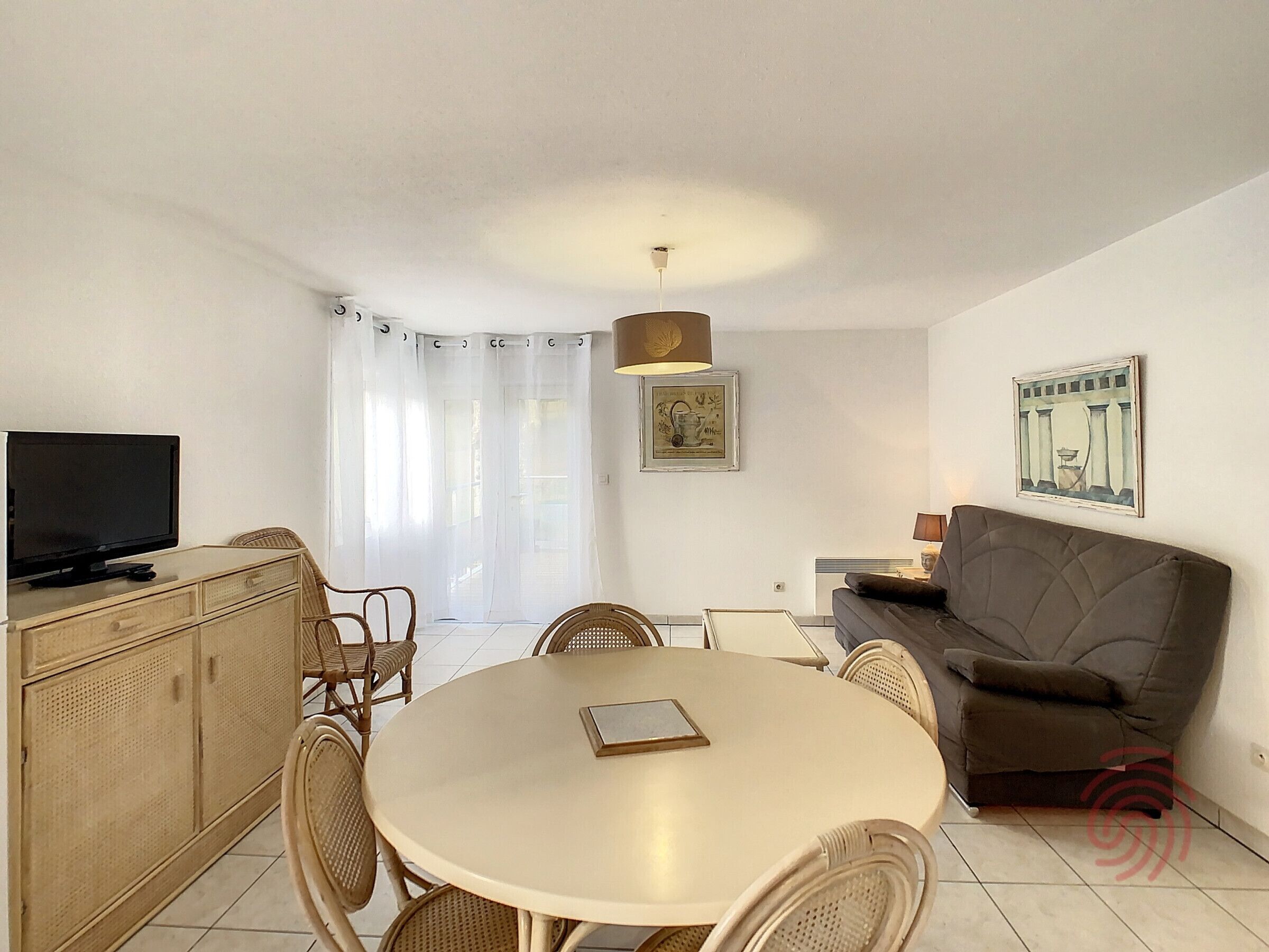 A living room with a round table, chairs, a sofa, a television, and a painting on the wall.