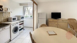 Eine kompakte Küche mit Waschmaschine, Mikrowelle und Kühlschrank. Es gibt eine Essecke mit Tisch und Stühlen sowie einen Fernseher auf einem Schrank.