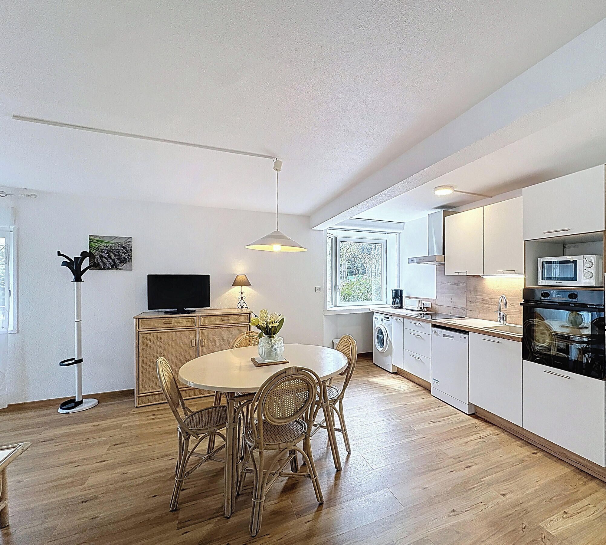 A modern kitchen with a dining area, wooden flooring, and a flat-screen TV.