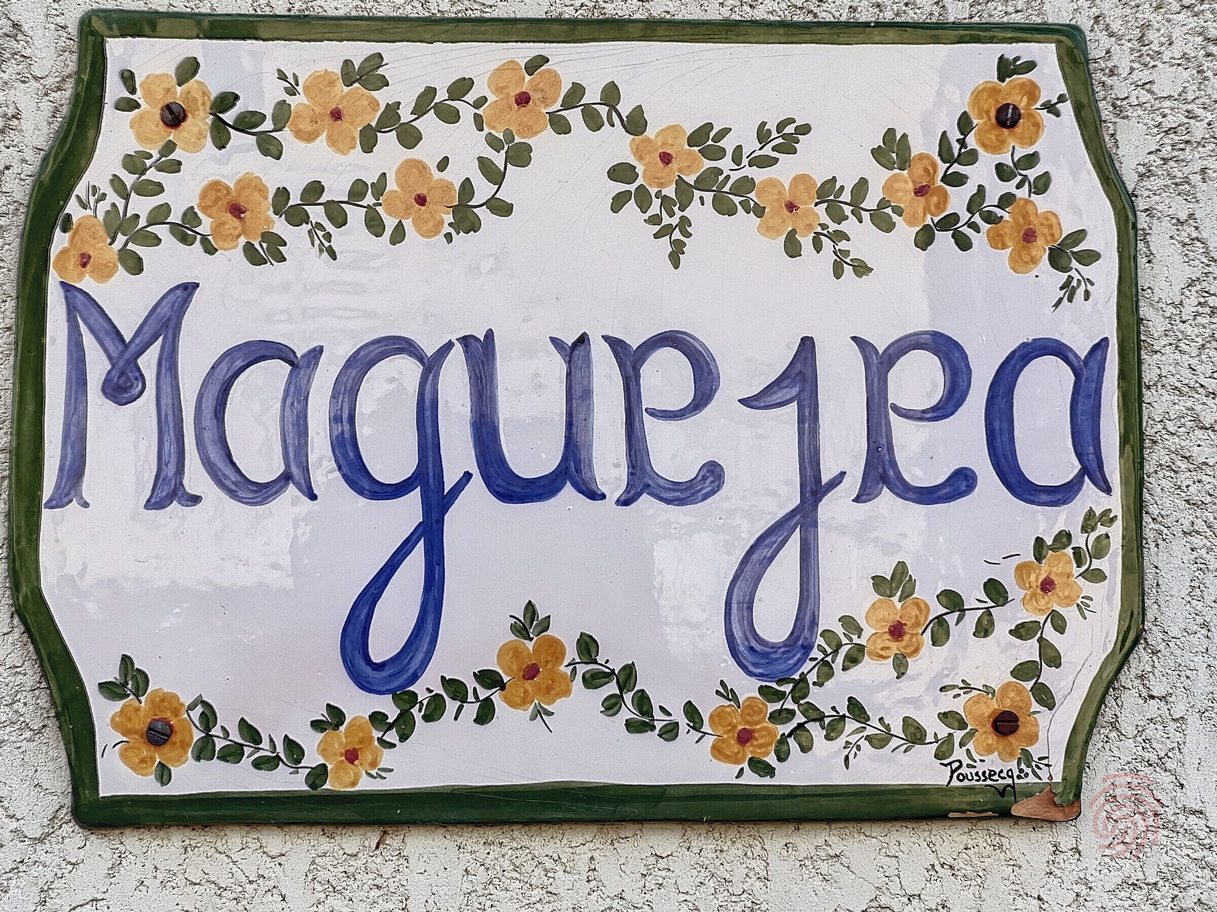 Een decoratief bord met de naam 'Magujeja', omringd door bloemdecoraties.