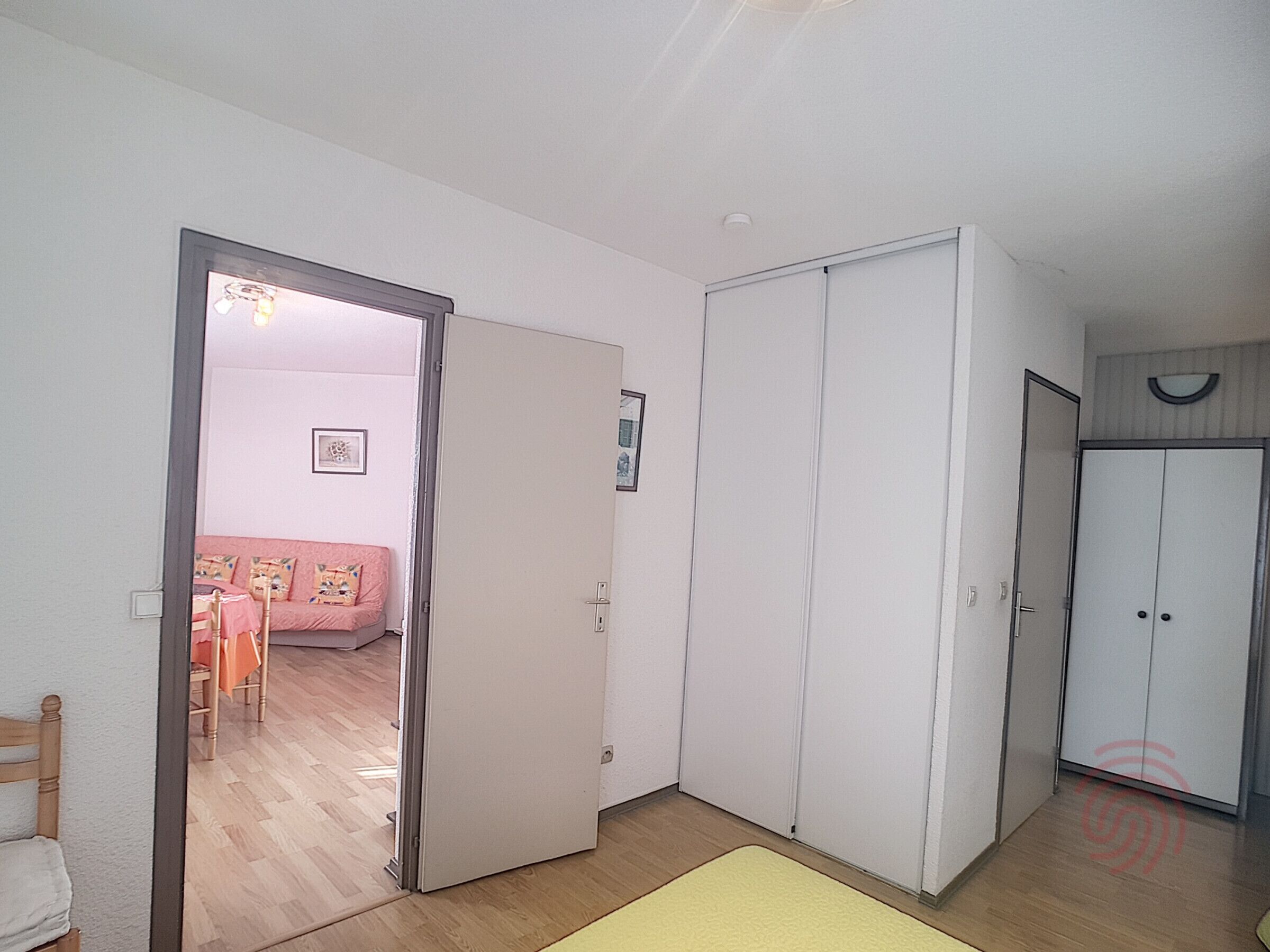 Una habitación con piso de madera, una cama con colcha rosa y un armario blanco.
