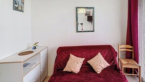 Ein Schlafzimmer mit Bett, Schminktisch, Stuhl, Spiegel und einem Fenster mit Vorhängen.