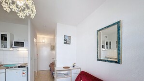 Ein gemütlicher Wohnraum mit Küchenzeile, einem roten Sofa, einem Spiegel und einer dekorativen Leuchte.