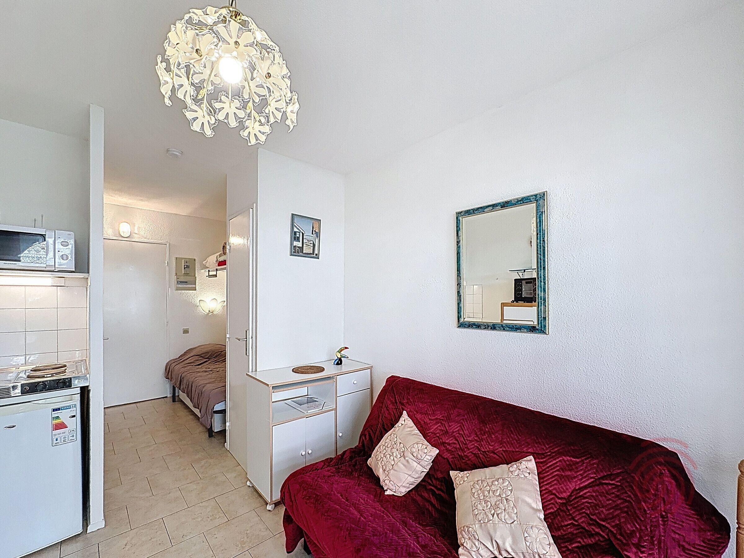 A compact room with a bed, a dresser, a microwave, a refrigerator, a mirror, and a decorative light fixture.