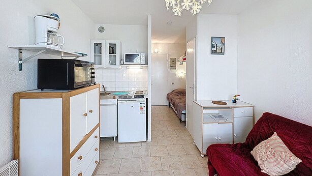 Eine kompakte Küche mit Mikrowelle, Toaster und Kühlschrank. Ein Bett mit roter Decke und ein kleiner Tisch mit Lampe sind ebenfalls vorhanden.