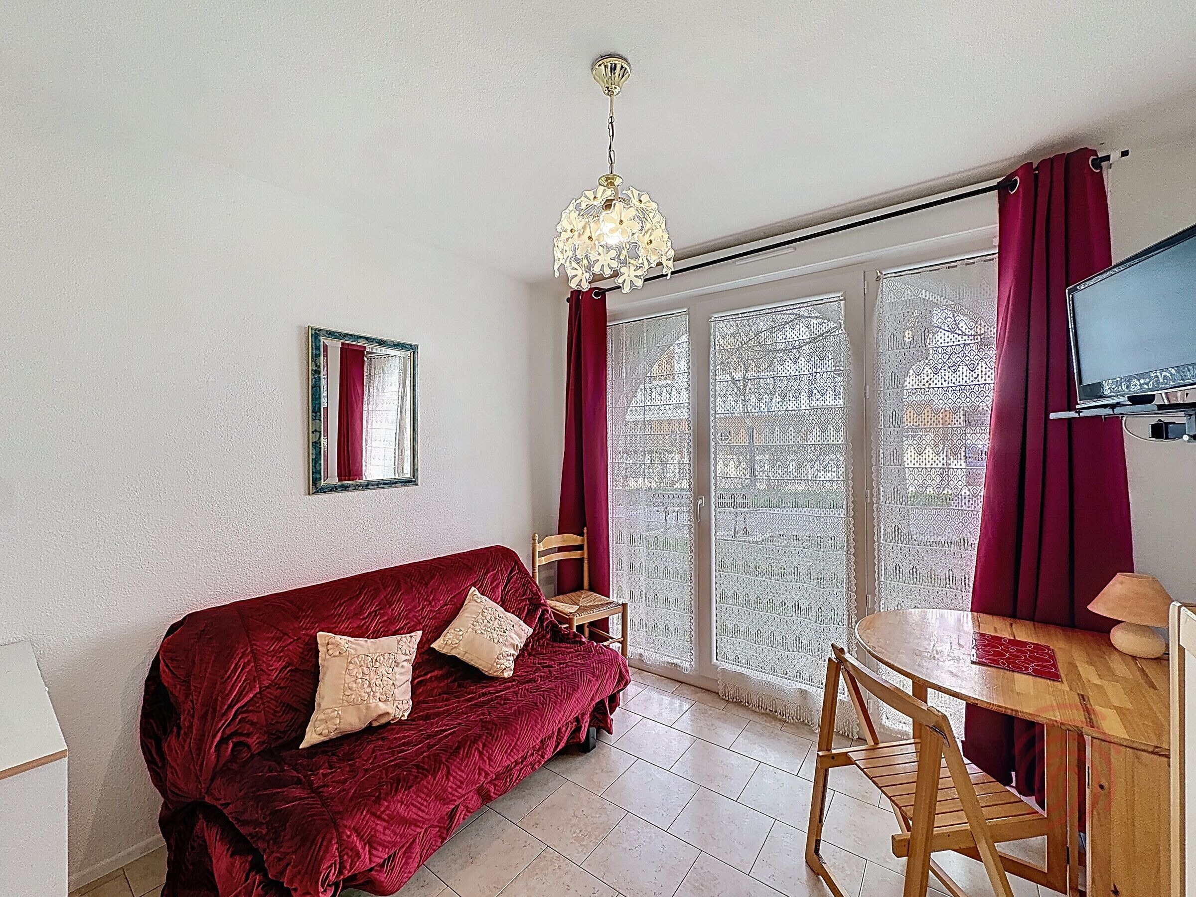 Una habitación con sofá rojo, una mesa de comedor de madera, televisor y ventana con diseño.