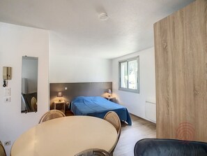 A room with a bed, a table, chairs, a lamp, a mirror, a phone, and a window.