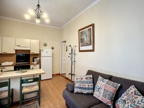 Un espace de vie compact comprenant un coin cuisine, un coin repas, un canapé agrémenté de coussins à motifs et un tableau accroché au mur.