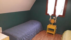 Een kleine eenpersoonskamer met schuine wand, houten vloer en een raam met gordijnen.