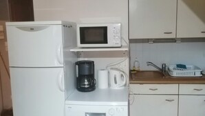 Una kitchenette compacta con refrigerador, microondas, cafetera y hervidor.