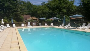 Una piscina rectangular con solárium alicatado, rodeada de sillas de descanso blancas y sombrillas.