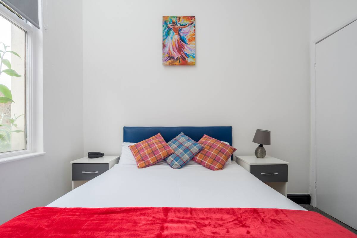 A modern bedroom with a large bed, colorful pillows, a blue headboard, and a painting above the bed.
