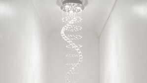 A modern chandelier with a spiral design hanging from a ceiling in a room with white walls.