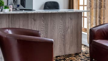 A reception area with a wooden desk, a computer, a clock, and two leather chairs.