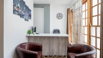 A room with a wooden desk, two leather chairs, a cityscape artwork, a clock, and a window with curtains.