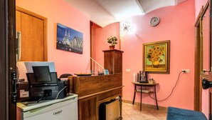 Una habitación con escritorio, impresora, mueble pequeño, silla, sofá azul, una pequeña mesa con un florero y un reloj en la pared.