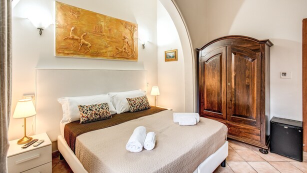 Una habitación de hotel con una cama, un armario de madera, un cuadro en la pared y una mesita de noche con una lámpara.