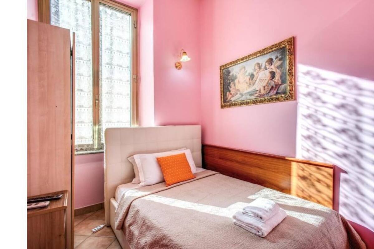 Un dormitorio con cama, mesita de noche, ventana y lámpara de pared.