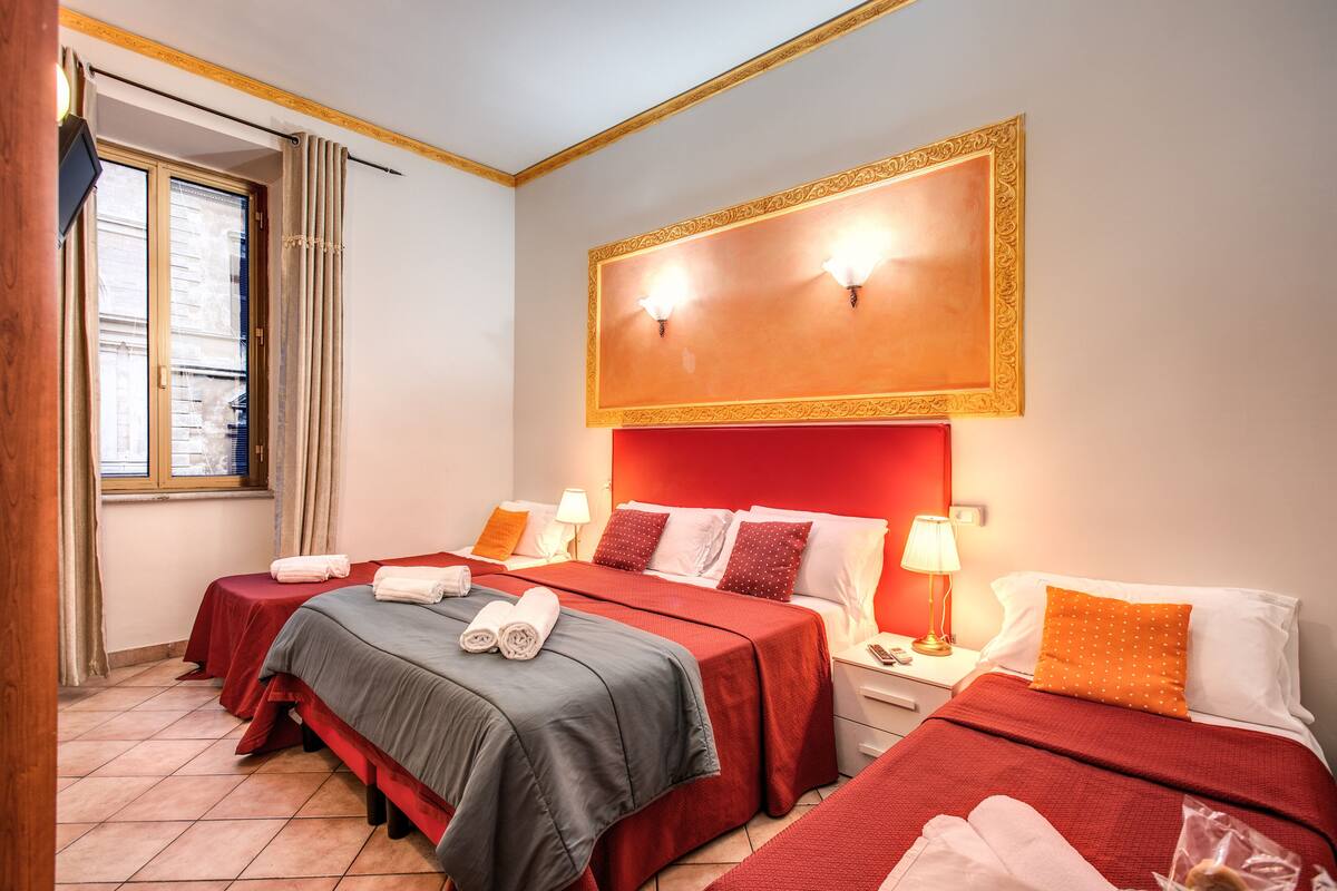 Una habitación de hotel con dos camas, una obra de arte enmarcadasobre las camas y una ventana con cortinas.