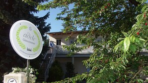 A sign for 'Adel Gastezimmer' with a logo, a building in the background, and a tree with red berries. - Adele - Gästezimmer am Elberadweg (Dresden)