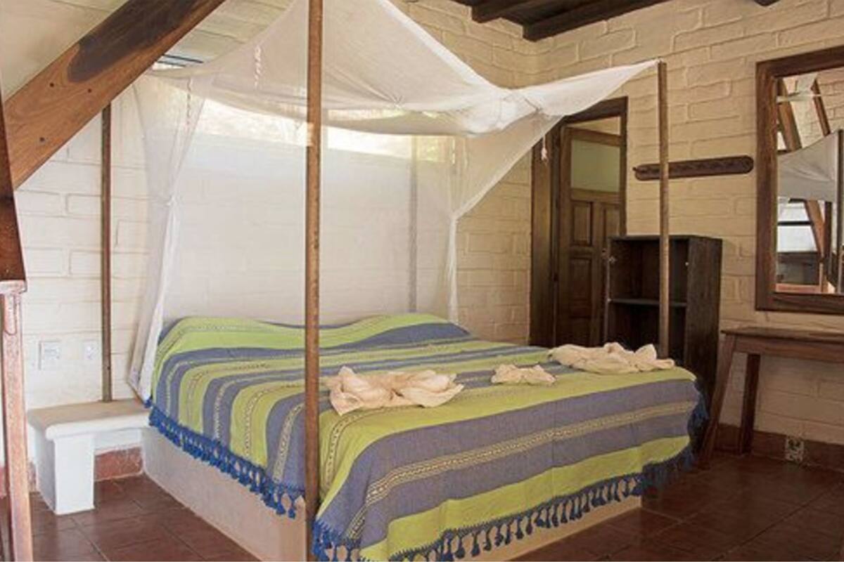 A room with a four-poster bed, a bench, a mirror, and a brick wall.