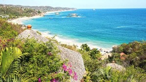 A coastal landscape with a beach, clear blue sea, and lush greenery. - Altamira Mazunte (Santa María Tonameca)