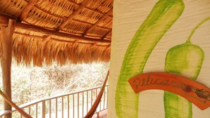 A hammock on a balcony with a thatched roof and a wall with a green chili pepper drawing and the word "Pelicana". - Altamira Mazunte (Santa María Tonameca)