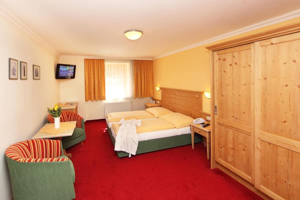 A hotel room with a bed, a desk, a chair, a wardrobe, and a television on the wall.