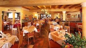 Ein Restaurant mit Holzbalken, Tischen mit weißen Tischdecken und einer Kristallleuchter.