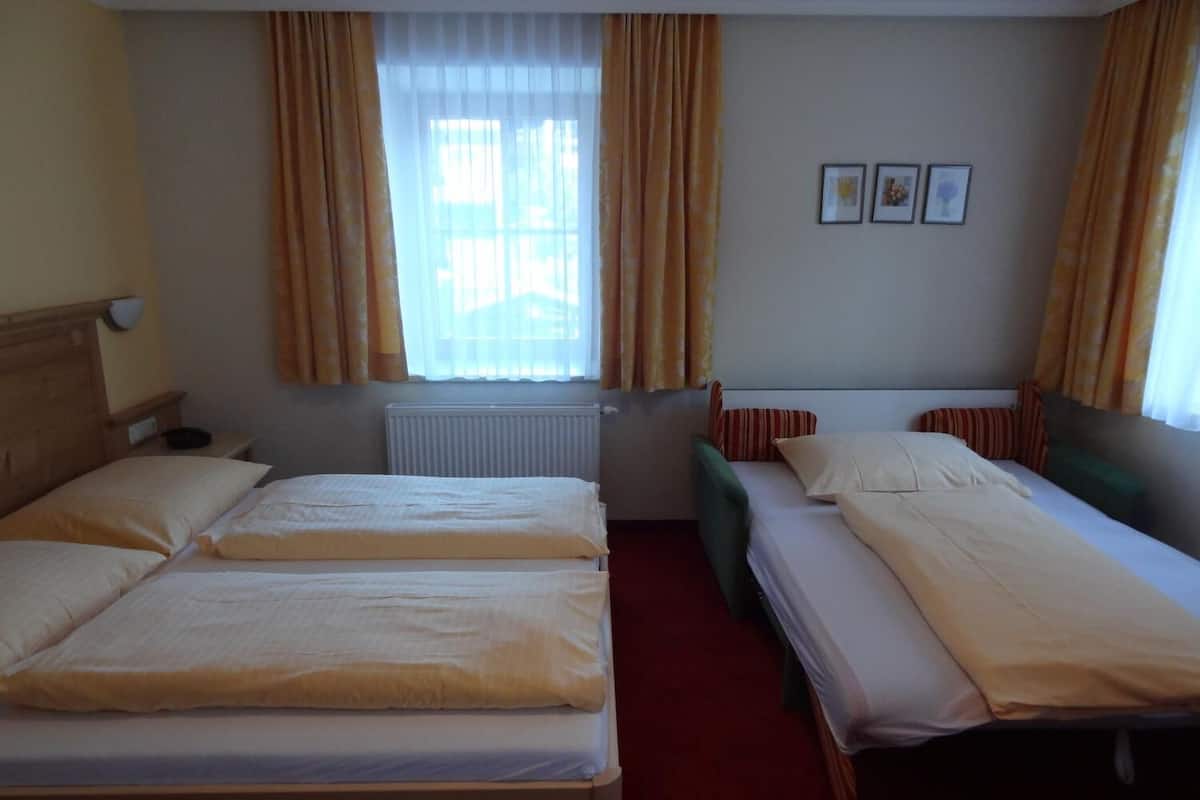 A hotel room with two beds, a radiator, a window with curtains, and a small table.