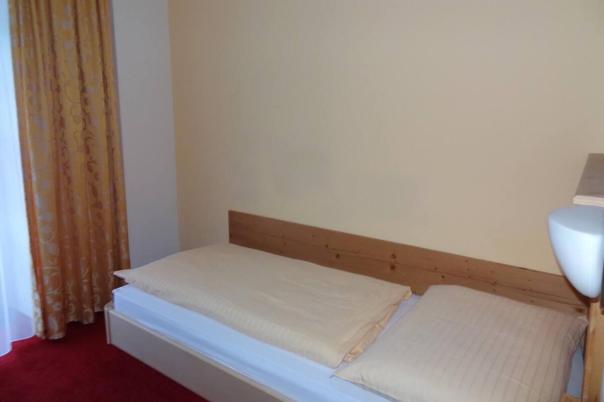 A single bed with a wooden headboard, a white bedside table, and a lamp on the right.
