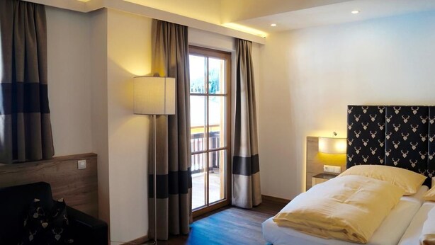 Ein Hotelzimmer mit Bett, Nachttisch, Lampe und Blick ins Freie durch ein Fenster.