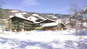Ein großes, mehrgeschossiges Hotel mit verschneitem Dach, umgeben von verschneiter Landschaft und Bergen.