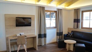 Ein modernes Zimmer mit einem Holztisch, einem schwarzen Ledersofa, einem runden Tisch und einem an der Wand befestigten Fernseher.