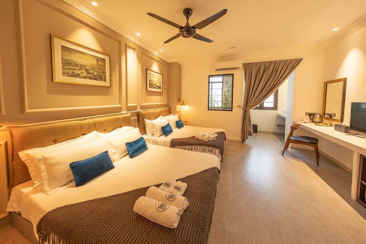 Une chambre d’hôtel avec deux lits, un bureau, une chaise, une télévision et un ventilateur de plafond.