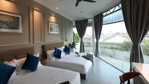 A hotel room with two beds, a ceiling fan, large windows with curtains, and artwork on the walls. - Reunion Residence (George Town)