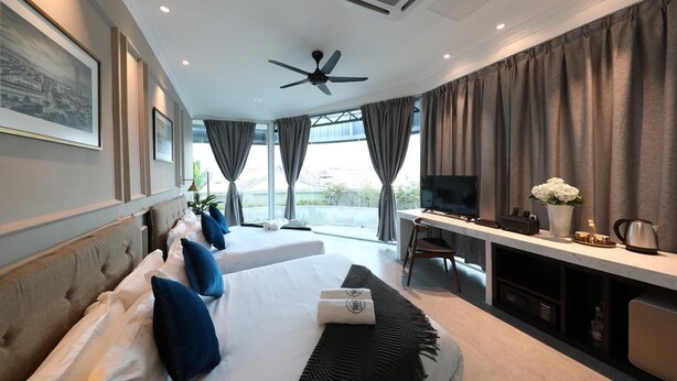A hotel room with two beds, a desk, a TV, and large windows with curtains. - Reunion Residence (George Town)