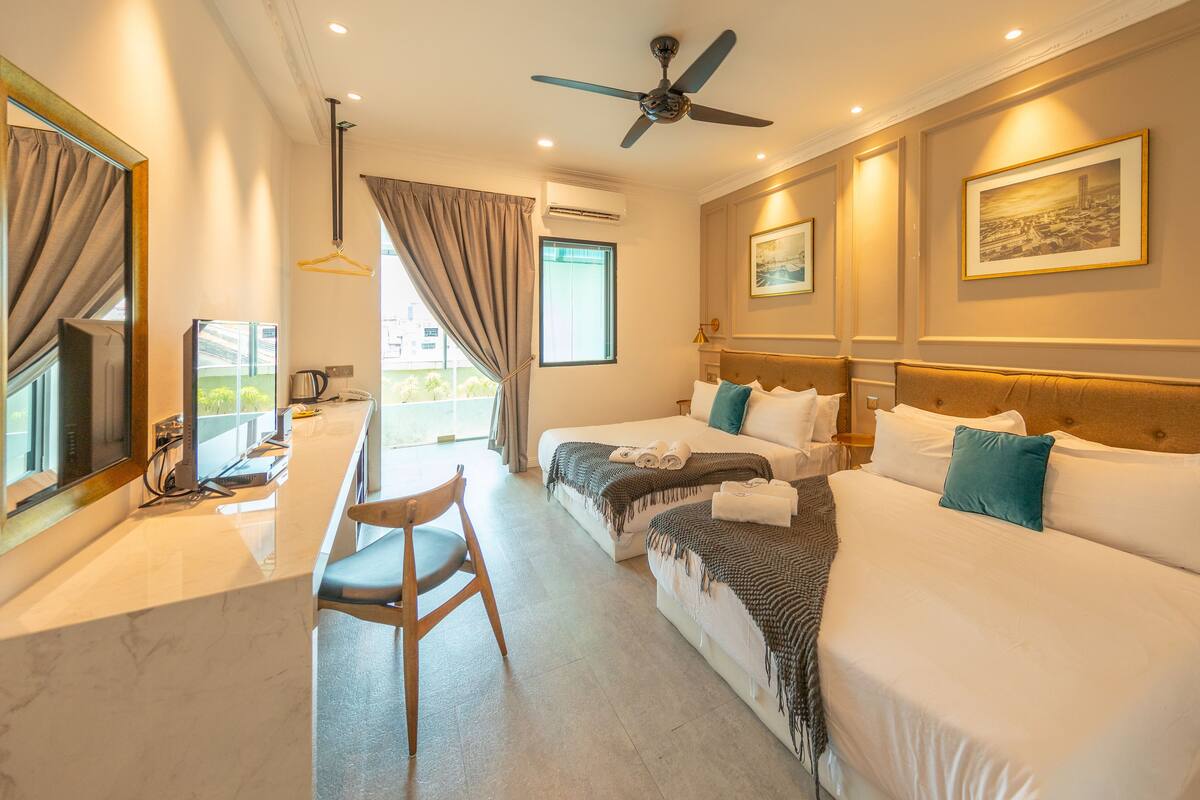 Une chambre d’hôtel équipée d’un lit, d’un bureau, d’une chaise, d’un ventilateur de plafond et d’une fenêtre avec des rideaux.