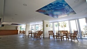 A spacious lobby with a high ceiling, large windows, and wicker furniture. - Oz Guzelcamli Otel (Kusadasi)