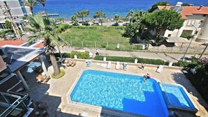 A swimming pool with a view of the sea, surrounded by palm trees and a few buildings. - Oz Guzelcamli Otel (Kusadasi)
