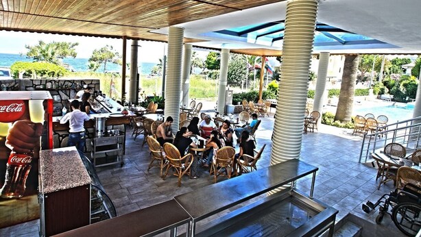 An outdoor dining area with tables and chairs, a Coca-Cola refrigerator, and a view of the ocean. - Oz Guzelcamli Otel (Kusadasi)