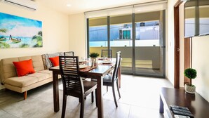 Un coin repas comprenant une table, des chaises et un canapé. Une fenêtre offre une vue sur les bâtiments environnants.