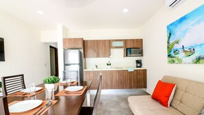 Une cuisine moderne avec des meubles en bois, un four à micro-ondes encastré et une machine à café. On y trouve une table à manger avec des chaises et un canapé agrémenté d’un coussin rouge.