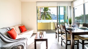 A modern living room with a sofa, dining table, chairs, and a view of the city through large windows. - The Furlough Fur201 (Playa del Carmen)