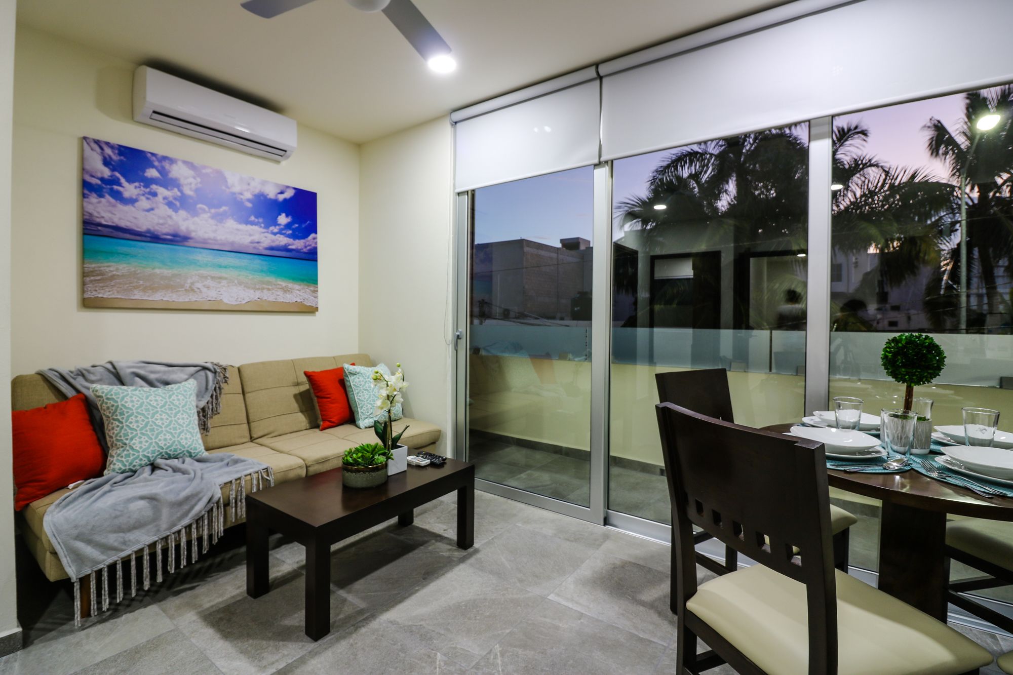 A modern living room with a beige sofa, a coffee table, and a dining area with a glass partition.