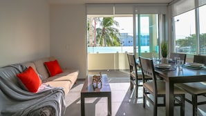 A modern living room with a sofa, a dining table with chairs, and a view of the city through large windows. - The Furlough Fur204 (Playa del Carmen)