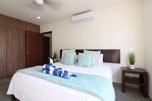 A bedroom with a large bed, a wooden wardrobe, an air conditioner, and a small bedside table with a plant.