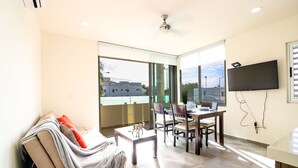 Un salon moderne avec un canapé, une table à manger et des chaises. Un téléviseur est fixé au mur et un ventilateur de plafond est installé.